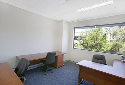 Private office suite with two timber desks, ergonomic chairs, and a large window overlooking trees.