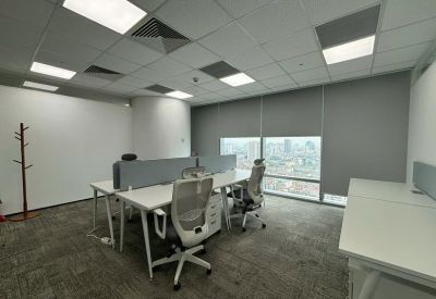 Modern open-plan office with white desks, ergonomic chairs, and a city view through large windows.