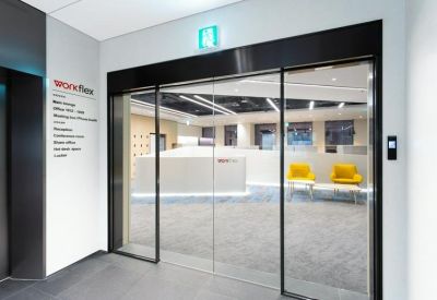 Modern office entrance with glass sliding doors and a white reception desk beyond.
