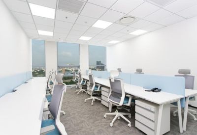 Bright open-plan office with white desks and ergonomic grey chairs near large windows.
