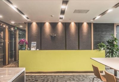 Minimalist yellow reception desk backed by dark textured wall panels and warm spotlighting.