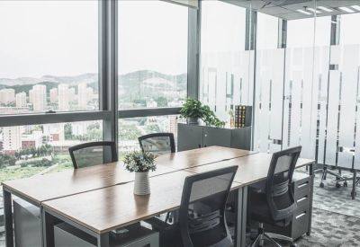 Bright coworking area with wooden desks and expansive city views through large windows.