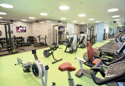 Modern fitness center with various cardio and weight machines on green flooring.