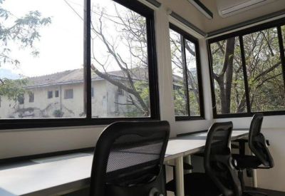 Bright office space with white desks and black chairs positioned near large windows.