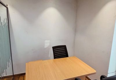 Small consultation room with a light wood desk and warm overhead cove lighting.