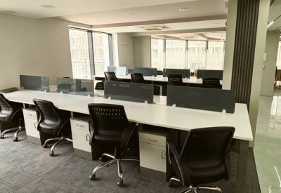 Bright coworking area with a long white desk and multiple black ergonomic chairs.