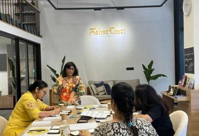 A presentation occurring in a bright common area with people seated around a light wood table.