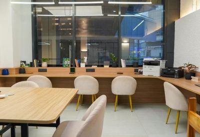 Brightly lit row of individual hot desks with plush velvet chairs and a printer station.