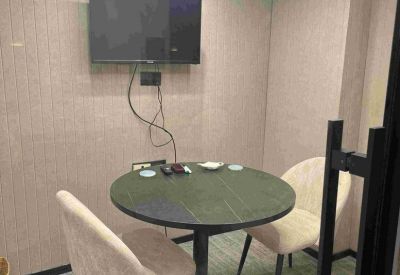 Private meeting pod with a round green table, wall-mounted TV, and acoustic wall panels.