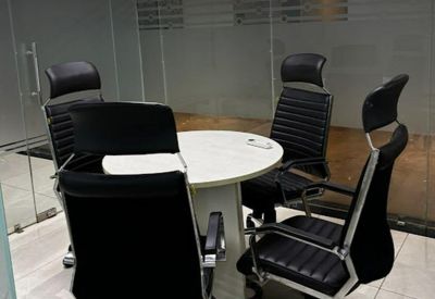 Small circular meeting table surrounded by four black ergonomic chairs behind a glass partition.