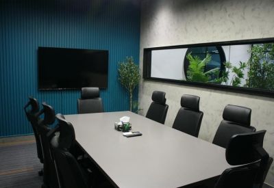 Well-lit meeting space with grey conference table, executive chairs, and a large wall monitor.