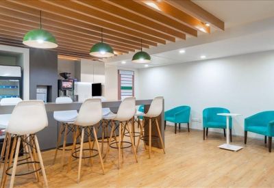 Vibrant breakroom with wooden ceiling slats, green pendant lights, and turquoise armchairs.