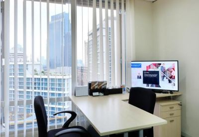 Private office with an L-shaped desk, city views through vertical blinds, and a monitor.