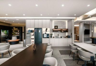 Communal kitchen area and breakout space with modern white cabinetry and a long dark dining table.