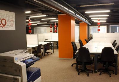 Coworking space featuring orange pillars, long white tables, and black chairs.