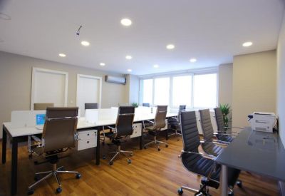 Bright open-plan workspace with wooden floors and several desks near large windows.