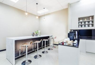 Modern breakroom with a white kitchen island, bar stools, and a coffee station.