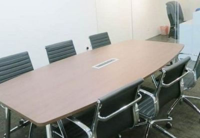 Modern conference room with a wooden table, black leather chairs, and a glass-walled reception area in the background.