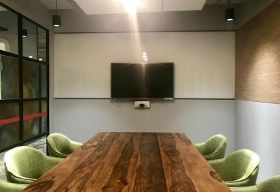Meeting room featuring a large natural wood table, green chairs, and a wall-mounted screen.