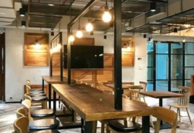 Coworking zone featuring high wooden tables, black bar stools, and industrial mesh ceiling panels.