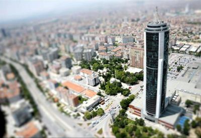 Aerial view of a modern skyscraper surrounded by city greenery and urban landscape.