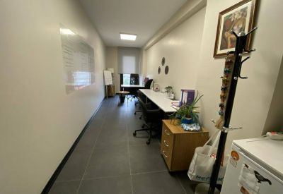 Narrow office space with long white desks, wooden storage units, and a coat rack.