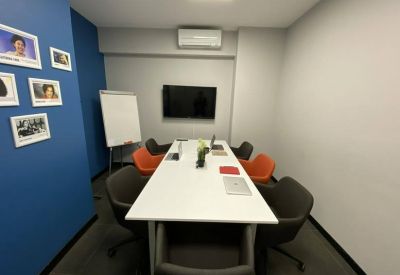 Meeting room with a white conference table, grey and orange chairs, and a wall-mounted TV.