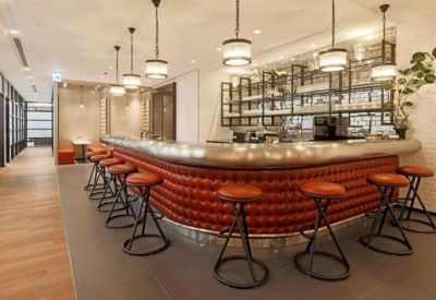 Modern curved bar and lounge area with red padded seating and industrial pendant lights.