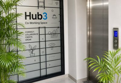 Reception area with branded glass partition, elevator, and potted palm trees.
