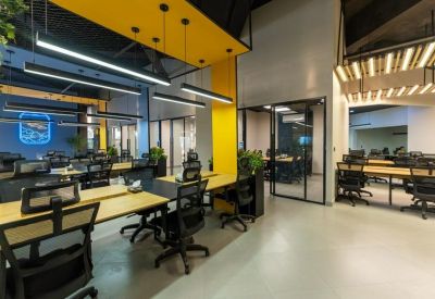 Modern open-plan office featuring yellow accent walls, industrial lighting, and several workstations.