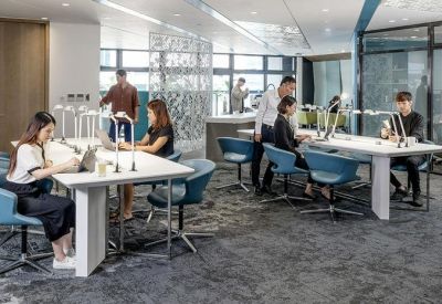 Open-plan office with multiple workstations, ergonomic blue chairs, and natural light.