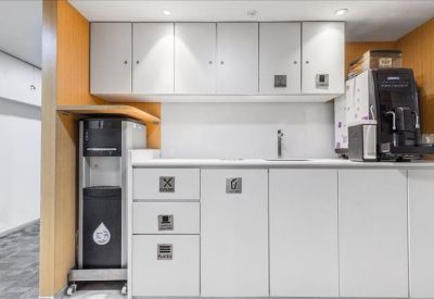 Clean communal kitchenette area featuring white cabinetry and a coffee machine.
