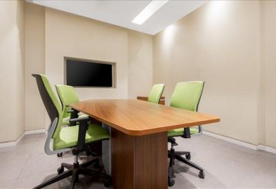 Compact meeting room with four green chairs, a wood-finish table, and a wall-mounted screen.