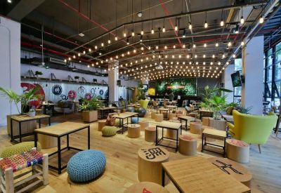 Spacious communal lounge with warm wooden floors, decorative hanging lights, and various colorful seating options.