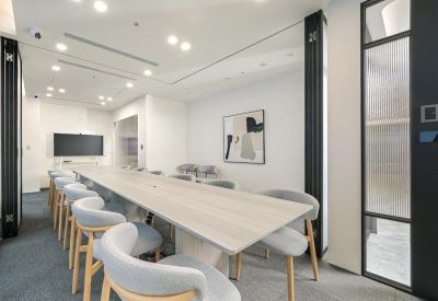 Professional boardroom with a long light wood table and gray upholstered chairs.