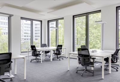Bright, modern open-plan office with white desks and black ergonomic chairs near tall windows.
