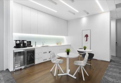 Sleek office kitchenette and coffee station with modern white cabinetry and small round tables.