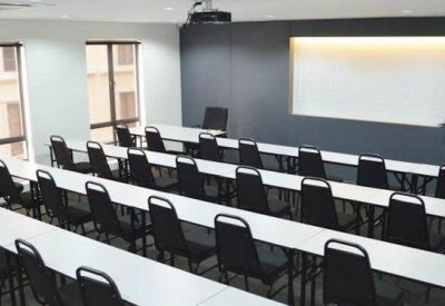 Lecture room with rows of tables and chairs facing a projector screen.