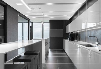Modern office kitchen and breakfast bar area with sleek white cabinetry and black stools.