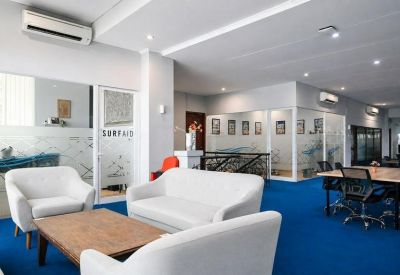 Modern lounge area with comfortable white armchairs, wooden coffee tables, and glass office partitions.