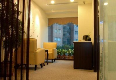 Reception waiting area with yellow armchairs, potted plants, and a dark wood front desk.