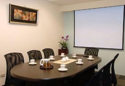 Meeting room with an oval dark wood table, several chairs, and a large projection screen.