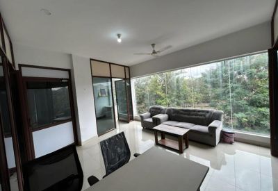 Lounge area with a grey sofa and a view through glass partitions into another office space.