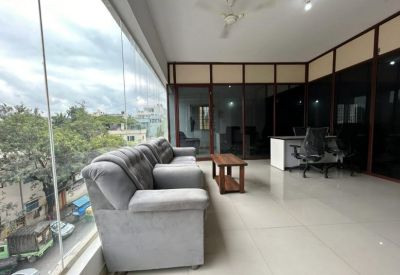 Sun-drenched breakout area with a plush grey sofa and floor-to-ceiling windows offering street views.
