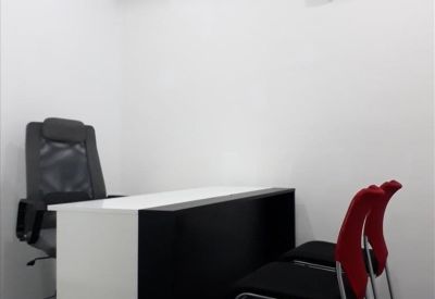 Modern workspace with a monochrome desk, black mesh task chair, and two red guest chairs.