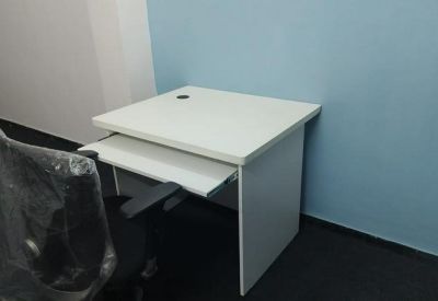 Single white workstation with a keyboard tray and black mesh chair against a blue wall.