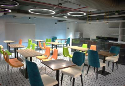 Cafeteria area with colorful green, blue, and orange chairs and square wooden tables.