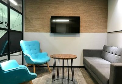 Small meeting area featuring bright turquoise armchairs, a wooden coffee table, and a wall-mounted TV.