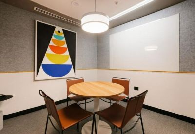 Modern four-person meeting room with a round wooden table and colorful geometric wall art.
