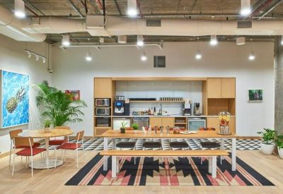 Spacious office kitchen and dining area with wooden tables, a patterned rug, and coffee station.